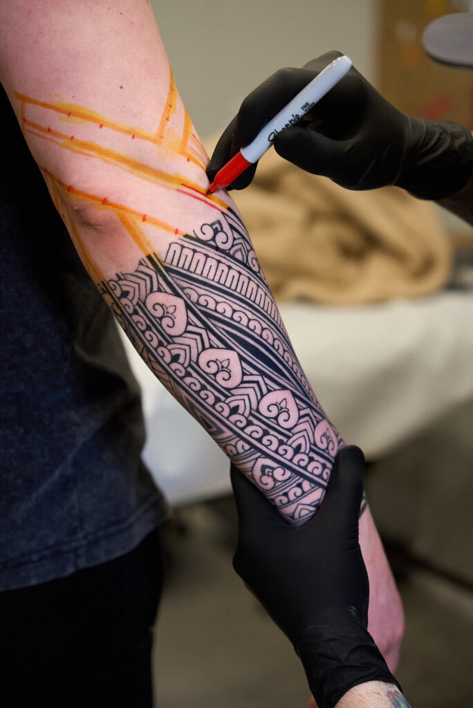 Tattoo artist outlining intricate design on client's forearm, showcasing detailed patterns for a planned tattoo sleeve at Inked Tattoo Studios.