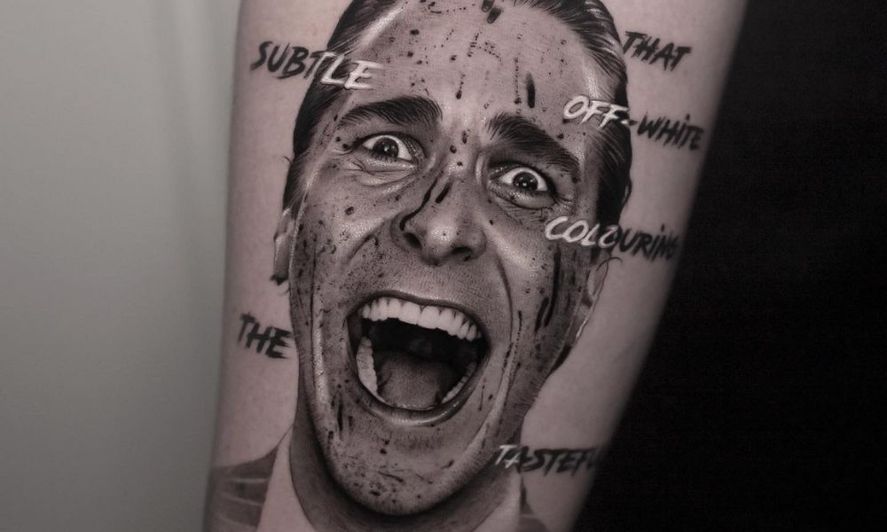 Tattoo of a smiling man with a splattered ink effect, featuring text elements like "SUBTLE," "OFF-WHITE," and "TASTEFUL," highlighting contemporary tattoo artistry trends.