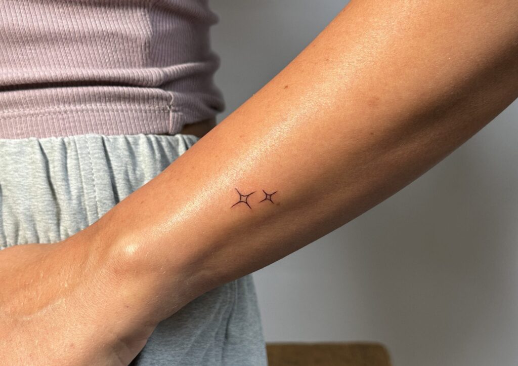 Two fine-line star tattoos on lower forearm