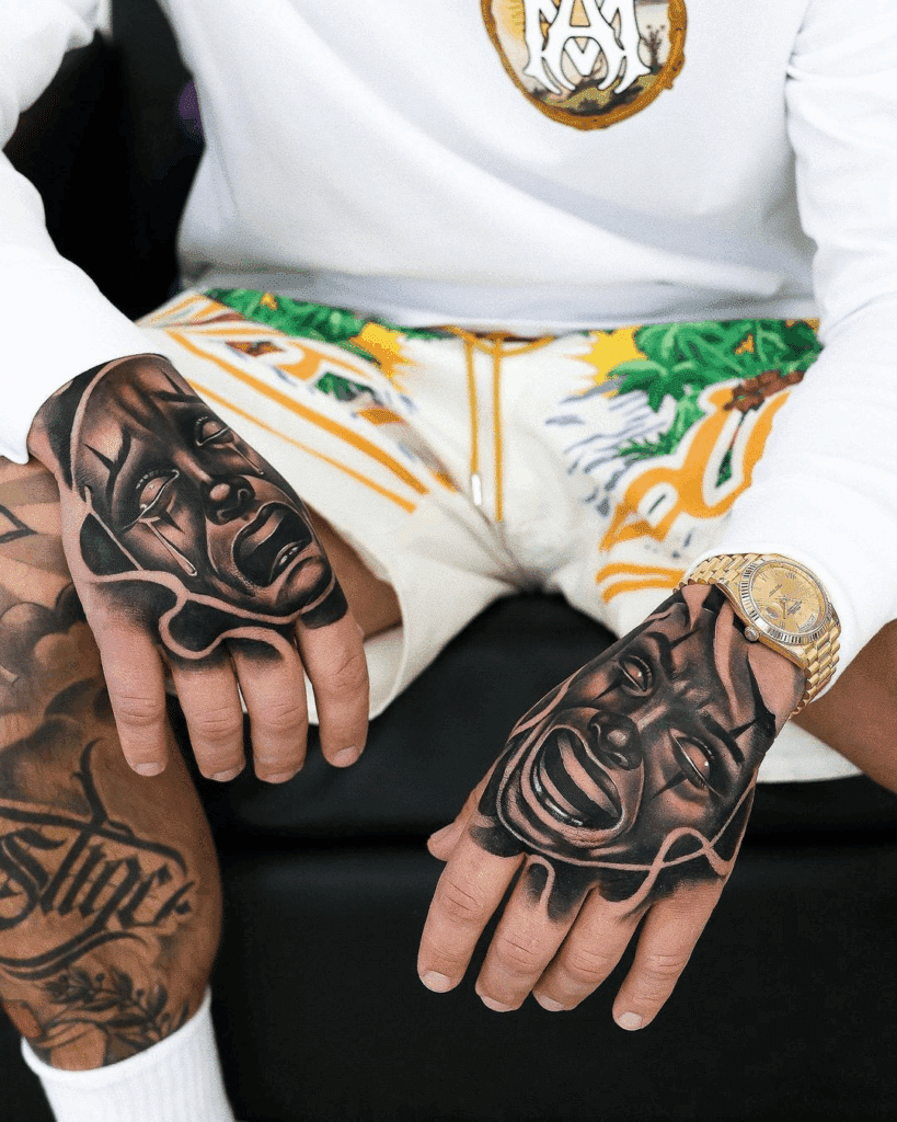 alt text: A pair of fresh black and grey tattoos on the tops of both hands, depicting dramatic faces with heavy shading 