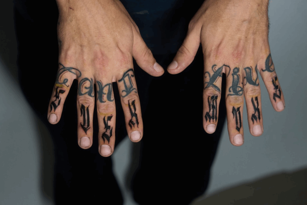 Close-up of both hands showing bold black script tattoos across the fingers