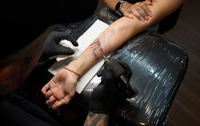 Woman in the process of getting a scorpion tattooed on the inner forearm