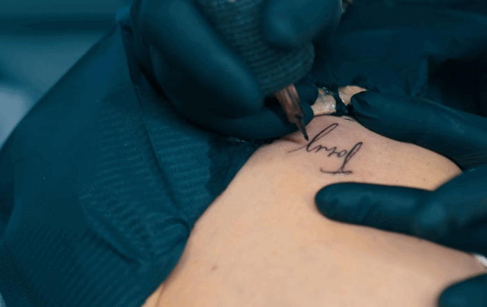 Close-up of artist in the process of tattooing a fine-line script tattoo on a client's ribs