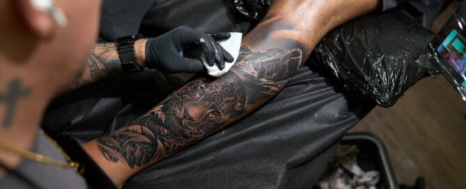 Black and grey tattoo on the lower leg featuring a jaguar, with an artist wiping the fresh tattoo.