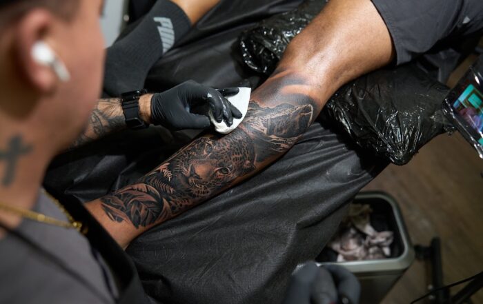 Black and grey tattoo on the lower leg featuring a jaguar, with an artist wiping the fresh tattoo.