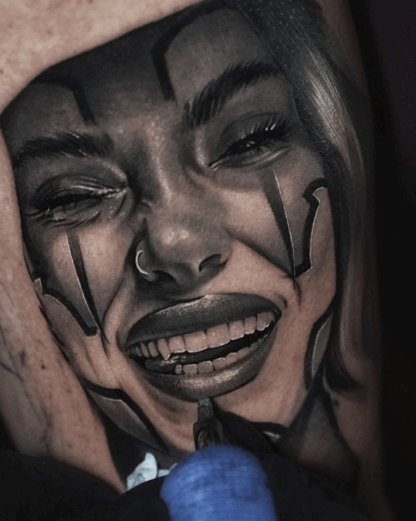 Black and grey realism tattoo of a woman’s face, showing fine shading detail as the artist works on her teeth and lips.