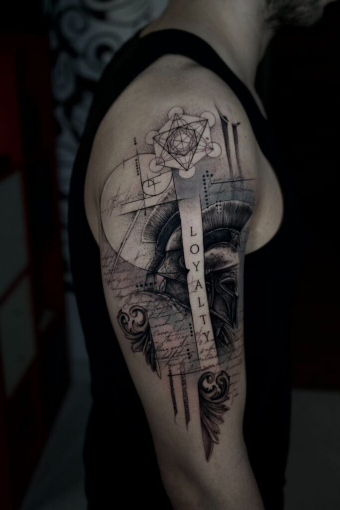 Black and grey upper arm tattoo with a Spartan helmet, geometric shapes, script, and the word “LOYALTY,” blending realism and geometric styles