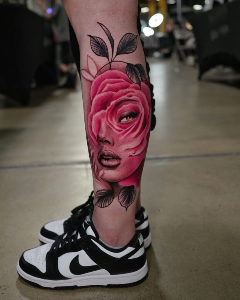 Realistic color tattoo on a person’s lower leg showing a pink rose that transforms into a woman’s face with leaves extending upward.