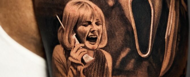 Black and grey upper-arm tattoo featuring the Ghostface mask from the movie “Scream” beside a woman holding a phone and screaming, with the text “Do you like scary movies” in dripping horror-style font.