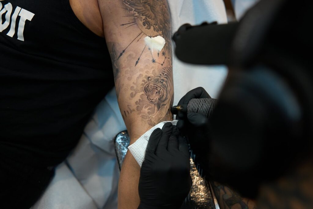 Close-up of a tattoo artist detailing a black and grey tiger design on a clientโs arm, captured mid-session.