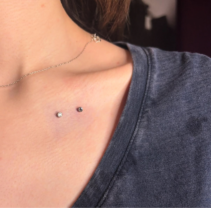Two dermal piercings on the upper chest of a person wearing a gray shirt and necklace.