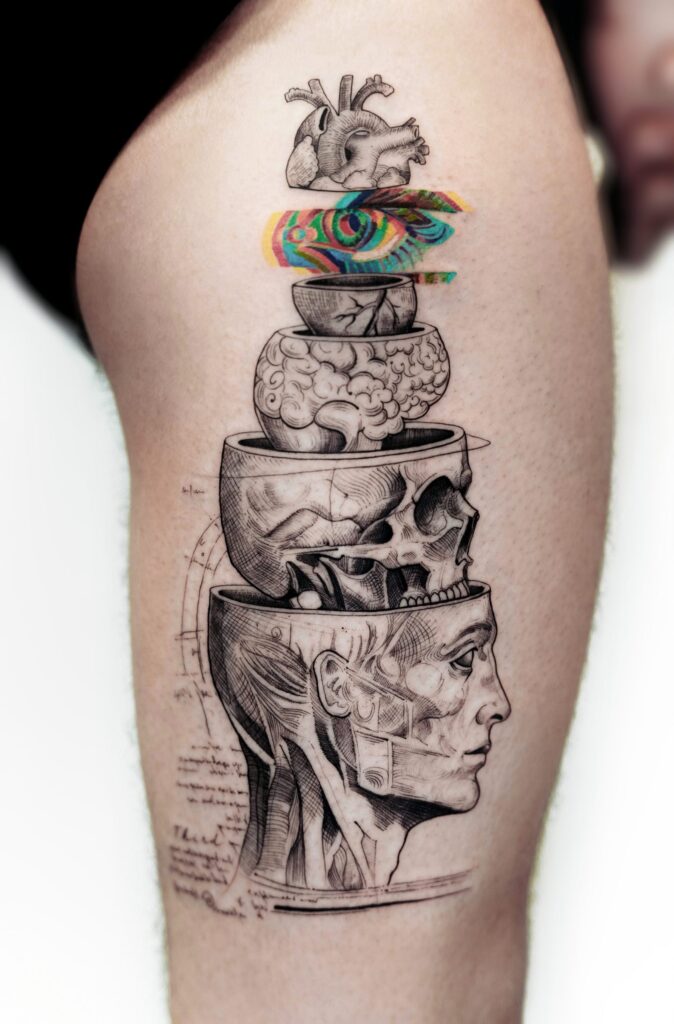 A thigh tattoo featuring an anatomical head rendered in stacked layers. Done in engraving style with a colorful abstract strip running horizontally through the top.