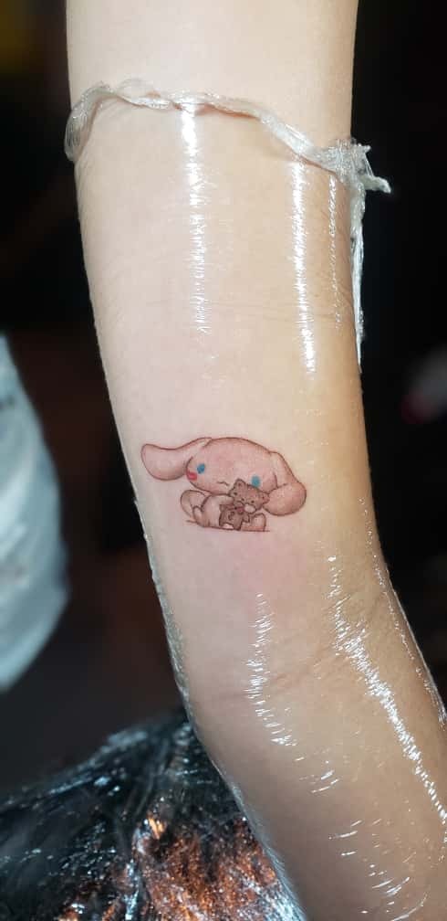 A small, pastel-colored tattoo of a cartoon bunny holding a teddy bear on the inner forearm, shown under protective wrap.