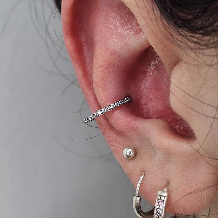 Close-up of an ear featuring a conch piercing with a silver gemstone-covered hoop, along with additional lobe piercings wearing silver jewelry.