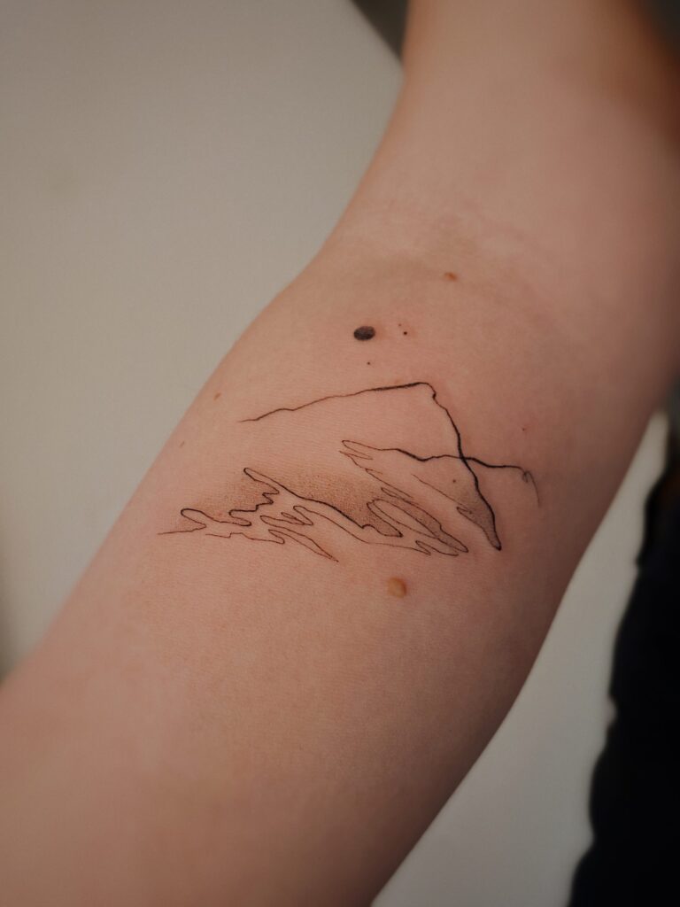 A abstract minimalist mountain landscape tattoo on the inner forearm.