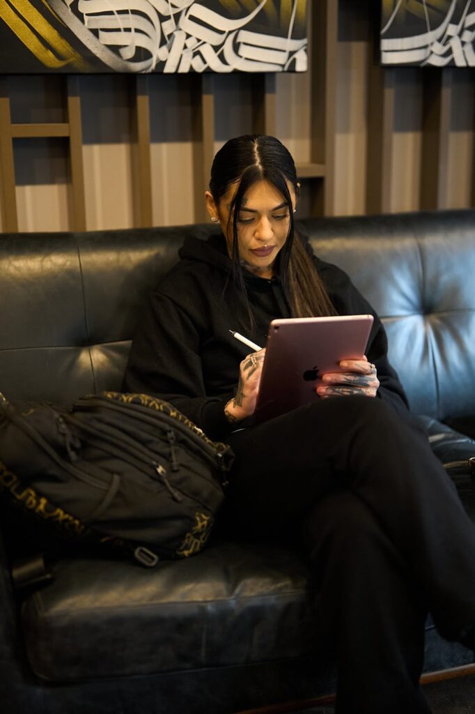 A tattoo artist sitting on a couch and drawing on a digital tablet in the studio.