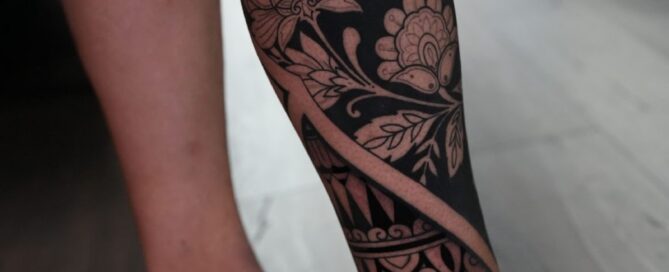 Leg tattoo combining blackout sections with intricate floral and ornamental linework