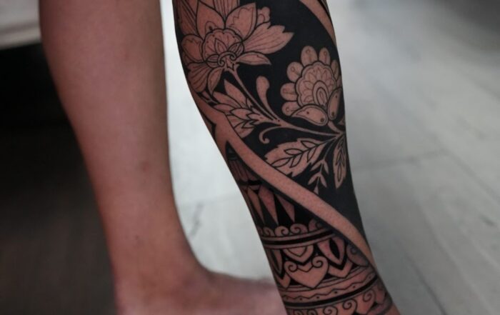Leg tattoo combining blackout sections with intricate floral and ornamental linework