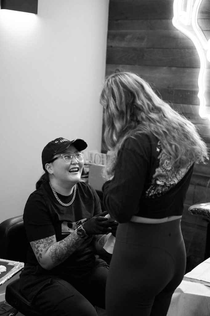 A tattoo artist wearing gloves smiling while consulting with a client in the studio.