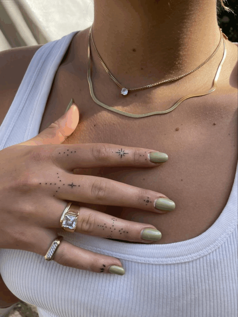 Small celestial tattoos on the fingers, including fine-line stars, dots, and minimalist symbols.