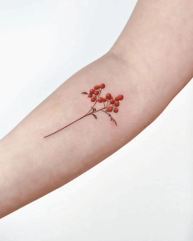 Tiny red berry branch tattoo on the inner forearm, featuring soft color shading and fine-line stems.