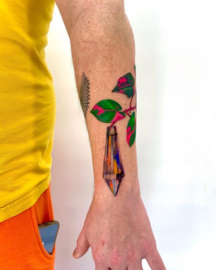 Colorful forearm tattoo of a faceted crystal with green and pink leaves, showcasing vibrant color saturation and fine line detail.