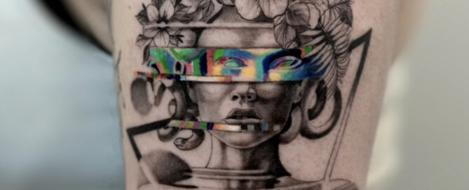 Black and gray upper arm tattoo featuring a surreal female bust with floral elements, geometric linework, and a colorful glitch-style band across the eyes.