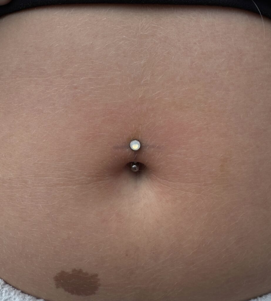 Close-up of a belly button piercing with a curved barbell featuring a small clear gemstone on the top end.
