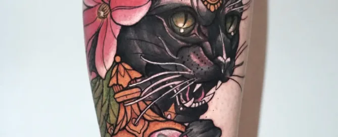 A detailed illustrative color tattoo on a leg, depicting a black panther with a jeweled headpiece holding a heart-shaped perfume bottle containing a goldfish.