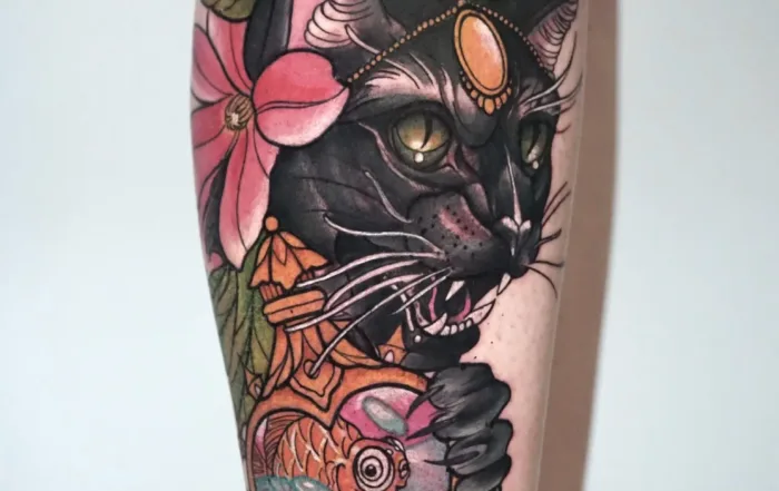 A detailed illustrative color tattoo on a leg, depicting a black panther with a jeweled headpiece holding a heart-shaped perfume bottle containing a goldfish.