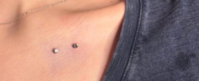 Close-up of two small dermal piercings placed on the upper chest near the collarbone, featuring minimal silver jewelry.