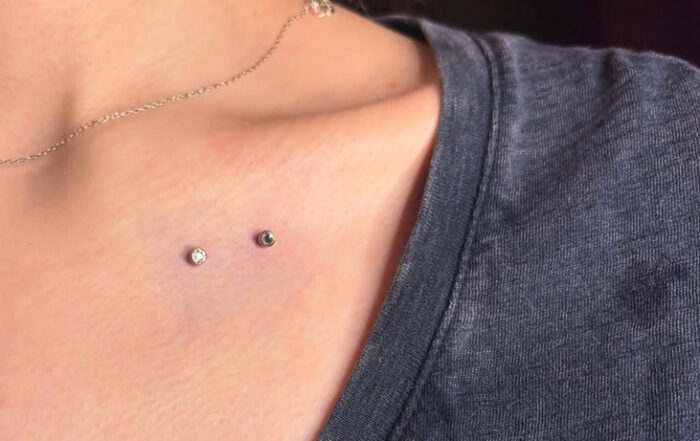 Close-up of two small dermal piercings placed on the upper chest near the collarbone, featuring minimal silver jewelry.