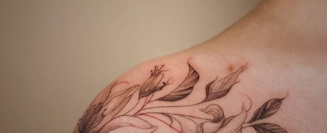 delicate, fine line floral tattoo across a female shoulders.