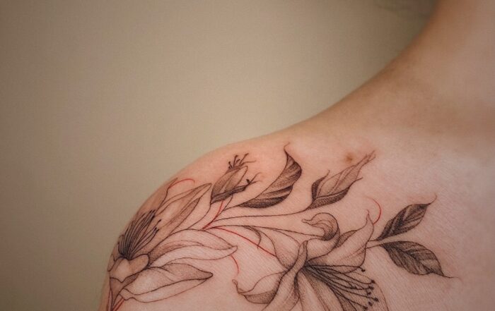delicate, fine line floral tattoo across a female shoulders.