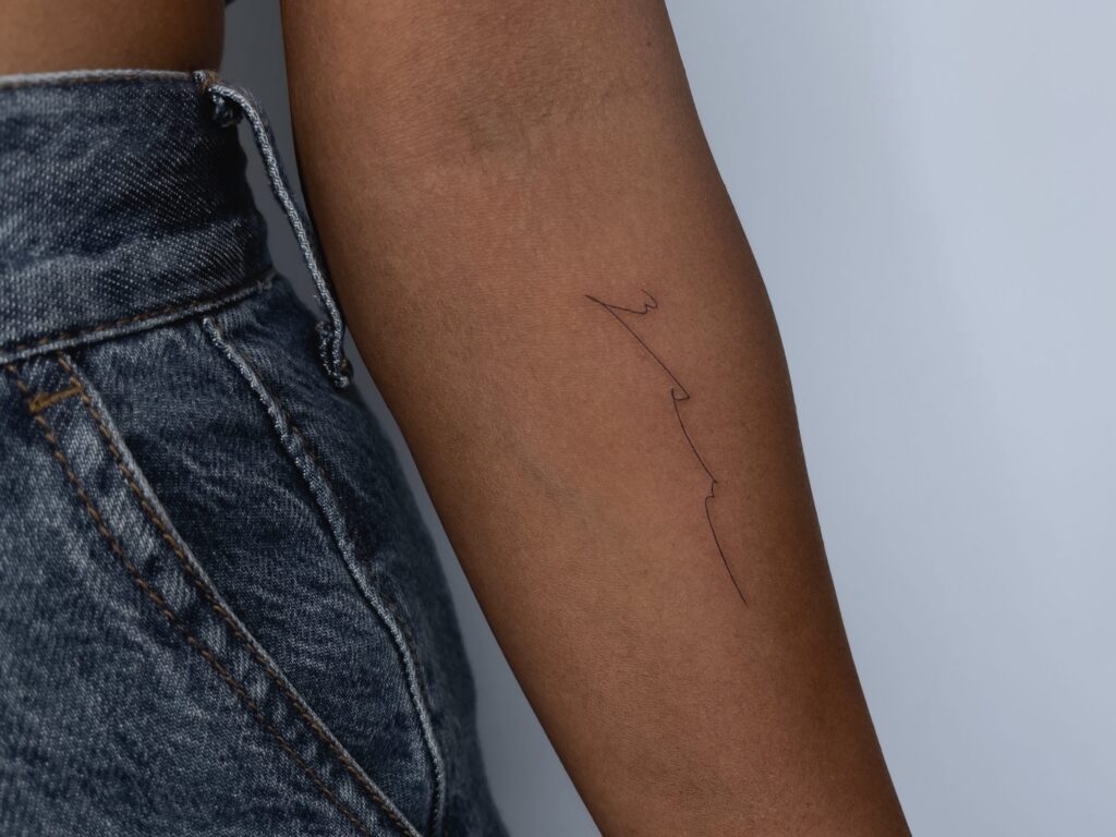 a fineline wave tattoo on a forearm