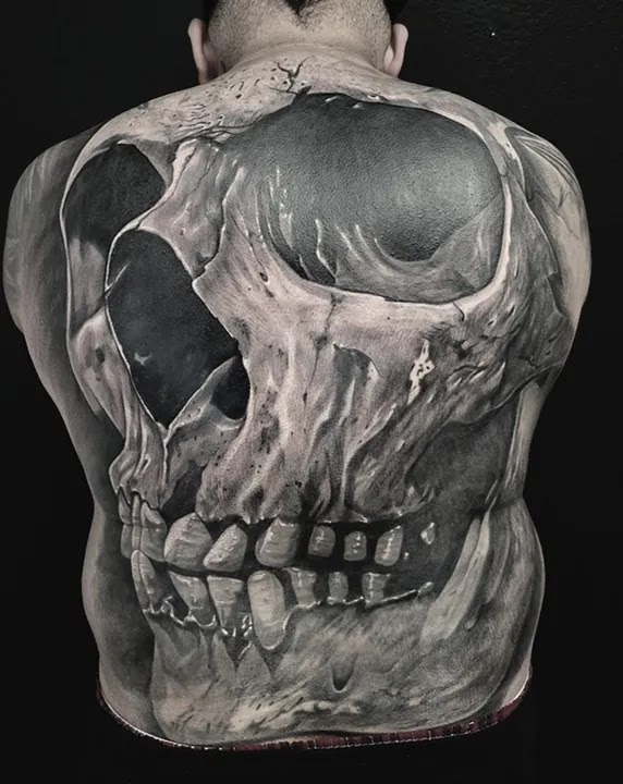 A large-scale, hyper-realistic black and grey tattoo of a skull covering the entirety of a person's back.