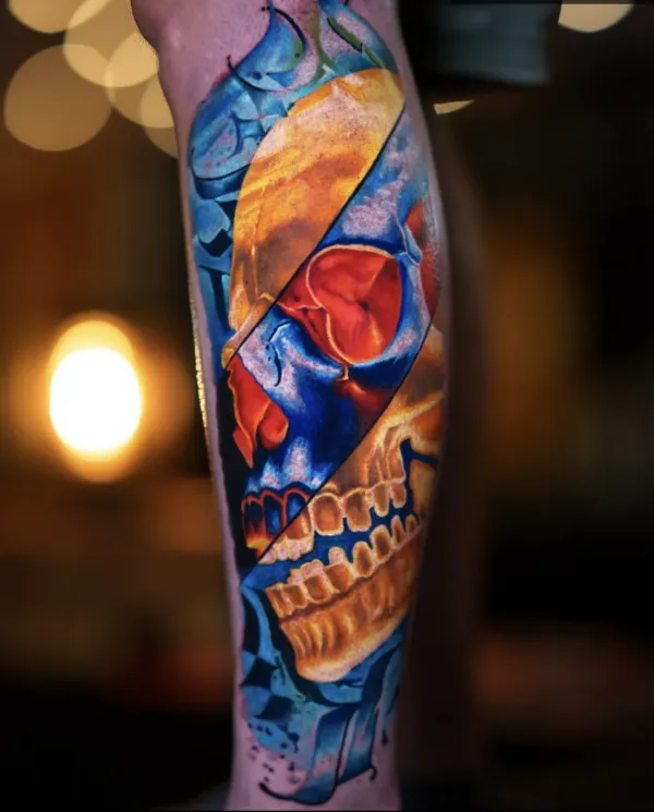 A vibrant, surrealist color realism tattoo on a leg. The design features a human skull divided into diagonal sections with a high-contrast color palette of electric blue, fiery orange, and deep red.