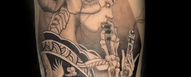 A detailed black-and-grey illustrative tattoo depicting a stylized woman in a traditional patterned kimono holding a katana. Her face is shown in profile, and a large, realistic human skull is integrated into her hair, creating a dark, surreal aesthetic.
