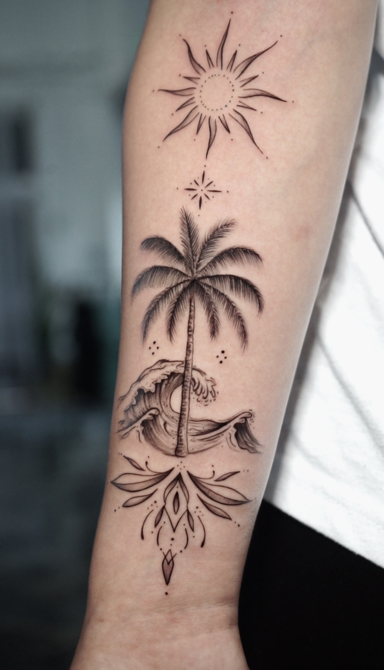 Delicate fine line black and grey forearm tattoo featuring a vertical geometric composition of a radiant sun, a detailed palm tree, crashing ocean waves, and ornamental linework.